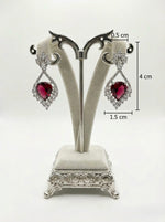 Pair of earrings with heart-shaped gemstones on a decorative stand with measurements.