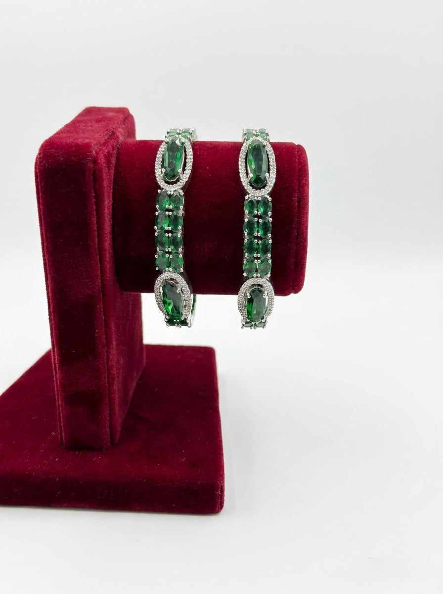 Pair of green gemstone earrings on a red velvet stand against a white background
