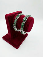 Pair of green gemstone hoop earrings on a red velvet stand against a white background