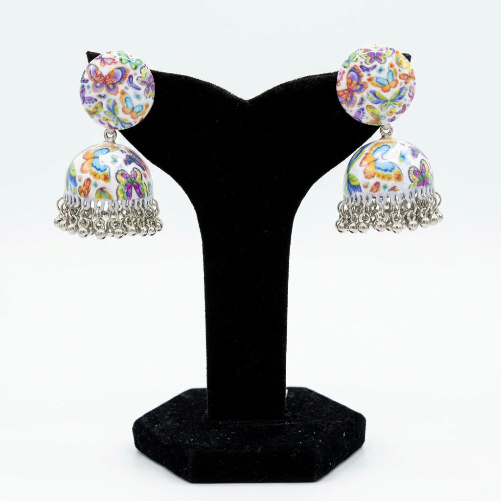 Pair of hand-painted white enamel jhumka earrings decorated with a colorful butterfly motif and dangling metallic beads.