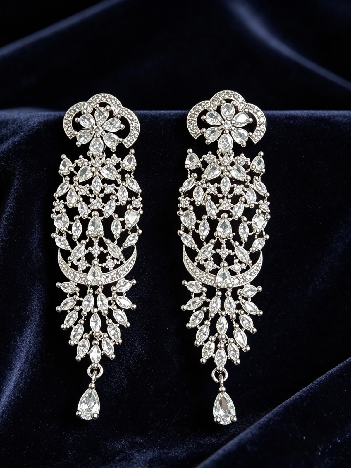 Pair of ornate diamond earrings on a dark fabric background
