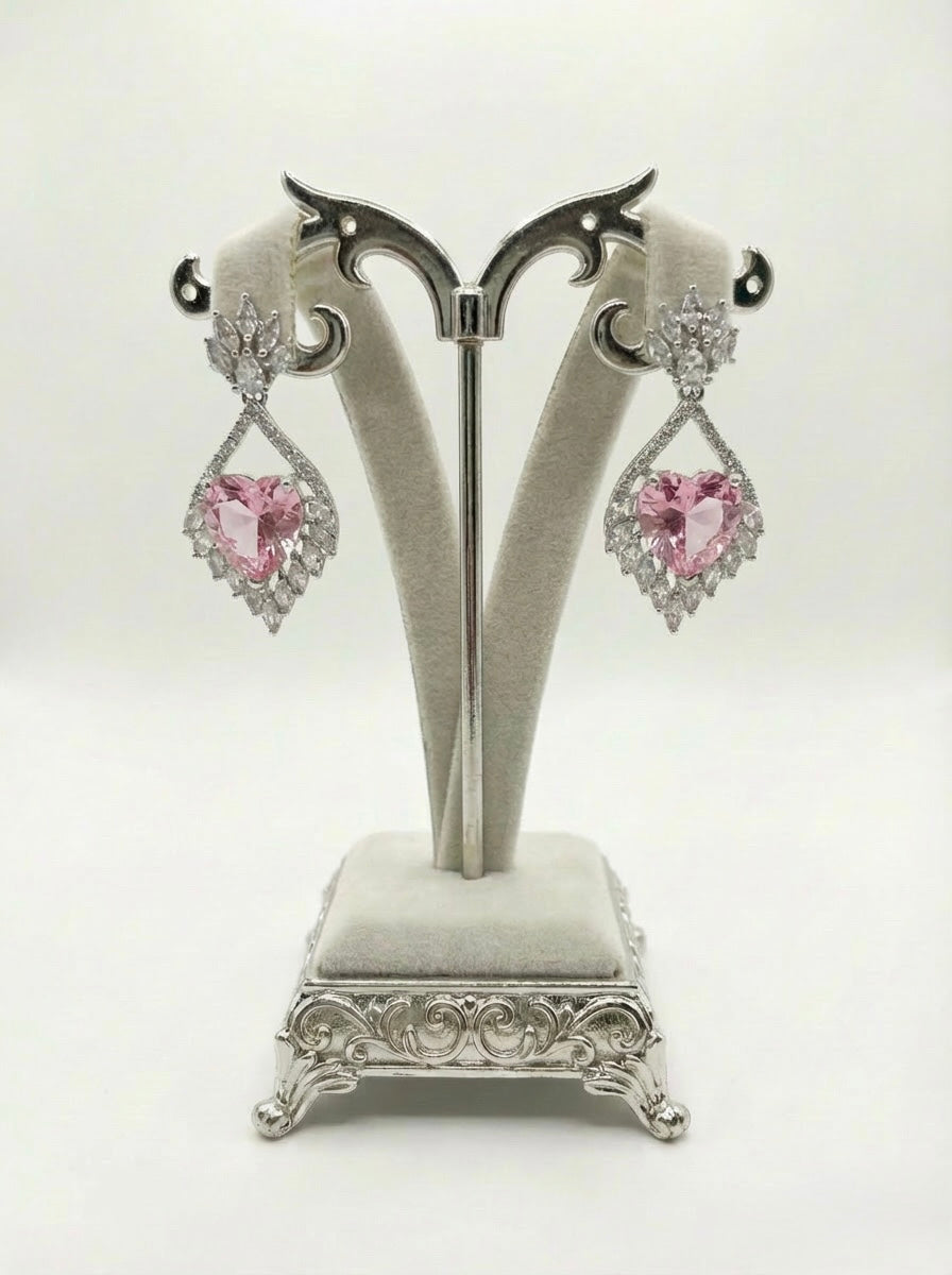 Pair of pink heart-shaped earrings on a decorative stand against a white background