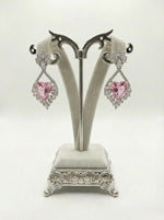 Pair of pink heart-shaped earrings on a decorative stand against a white background