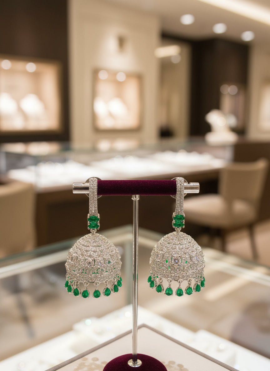 Pair of silver earrings with green gemstones on a stand in a jewelry store setting.