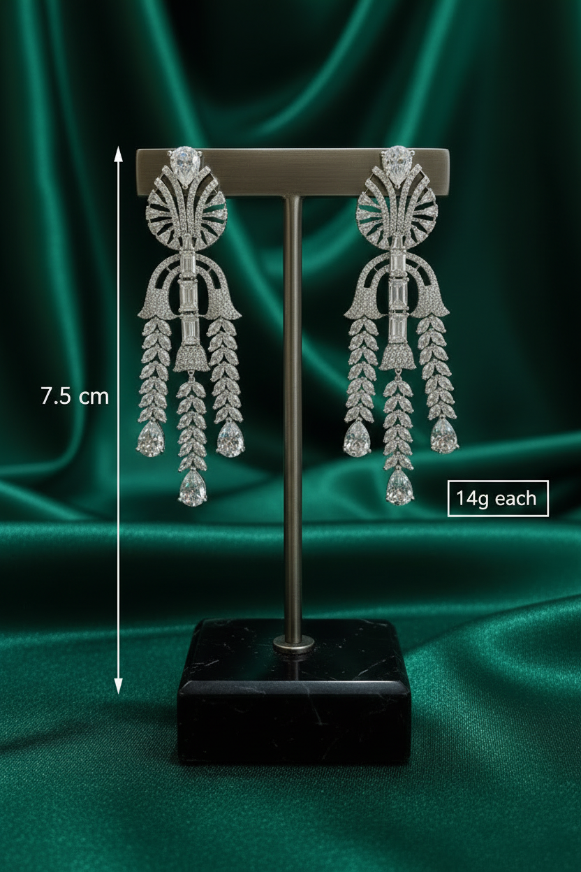 A pair of silver-toned Art Deco dangle earrings displayed on a black marble stand against a draped cream satin fabric background.