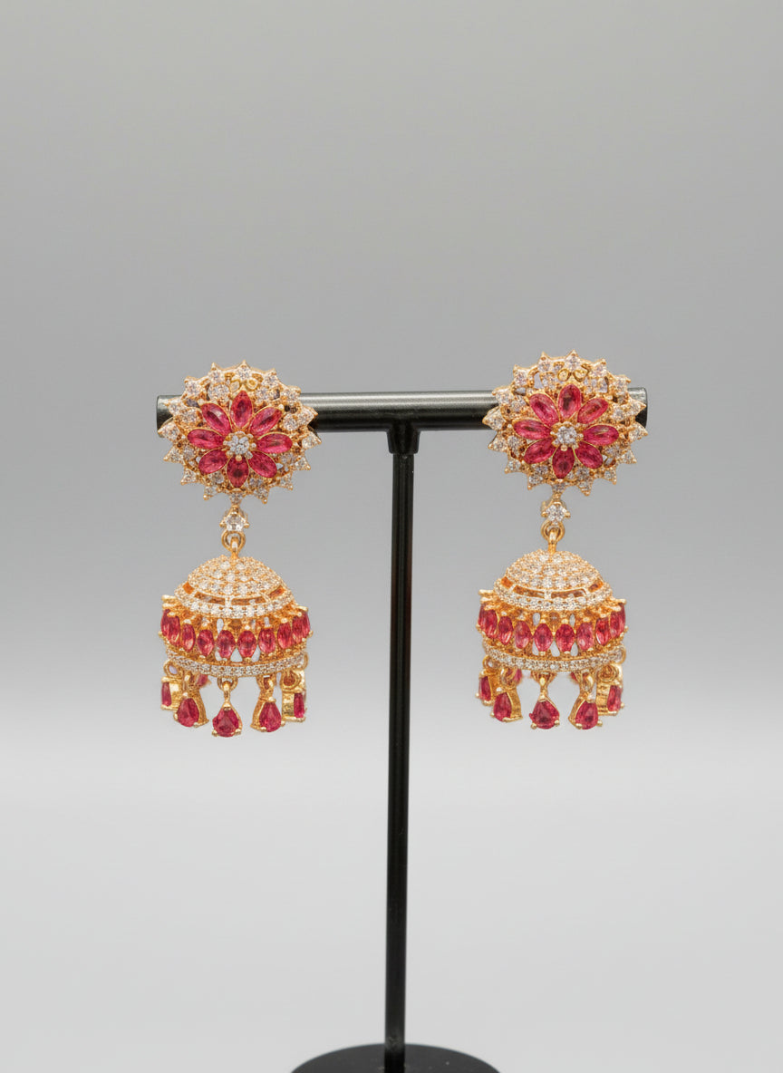 Party wear earrings. A pair of gold-plated jhumka earrings featuring hot pink rhinestones and a floral design. 