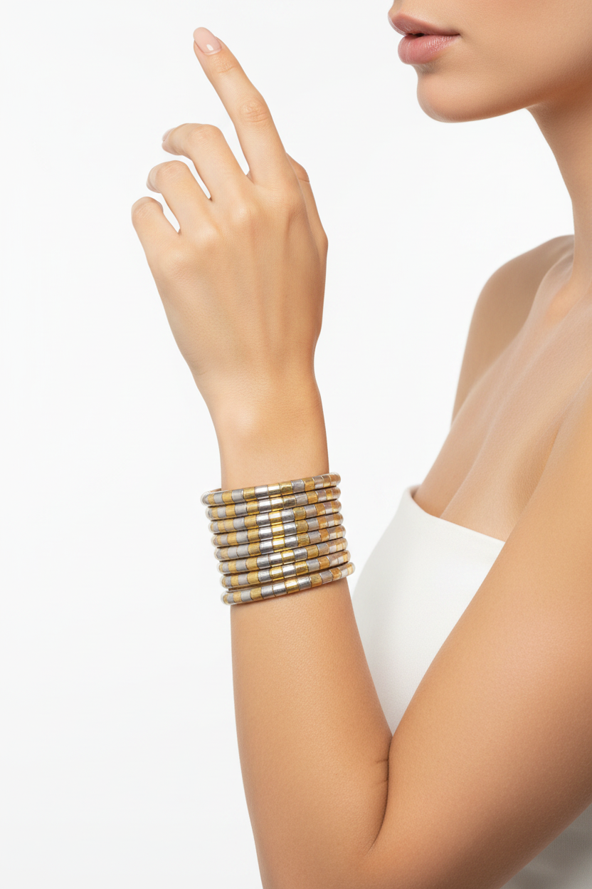 A close-up of a model's wrist wearing a stack of metallic bangles with a gold and silver striped pattern, set against a clean white background.