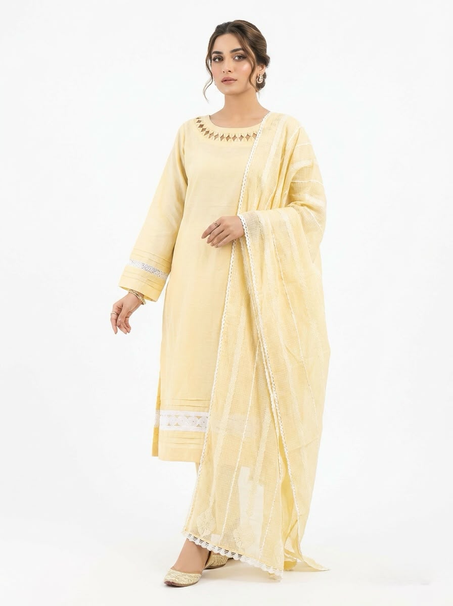 A model wearing a pastel yellow 3-piece cotton salwar kameez suit with a matching sheer dupatta. The kurta features geometric cutout embroidery along the neckline, pleated sleeves, and a white lace insert at the hem.