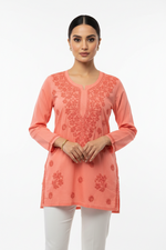 Peach cotton short kurti with intricate chikankari floral embroidery on neckline, yoke and cuffs, displayed on a model against plain white background.