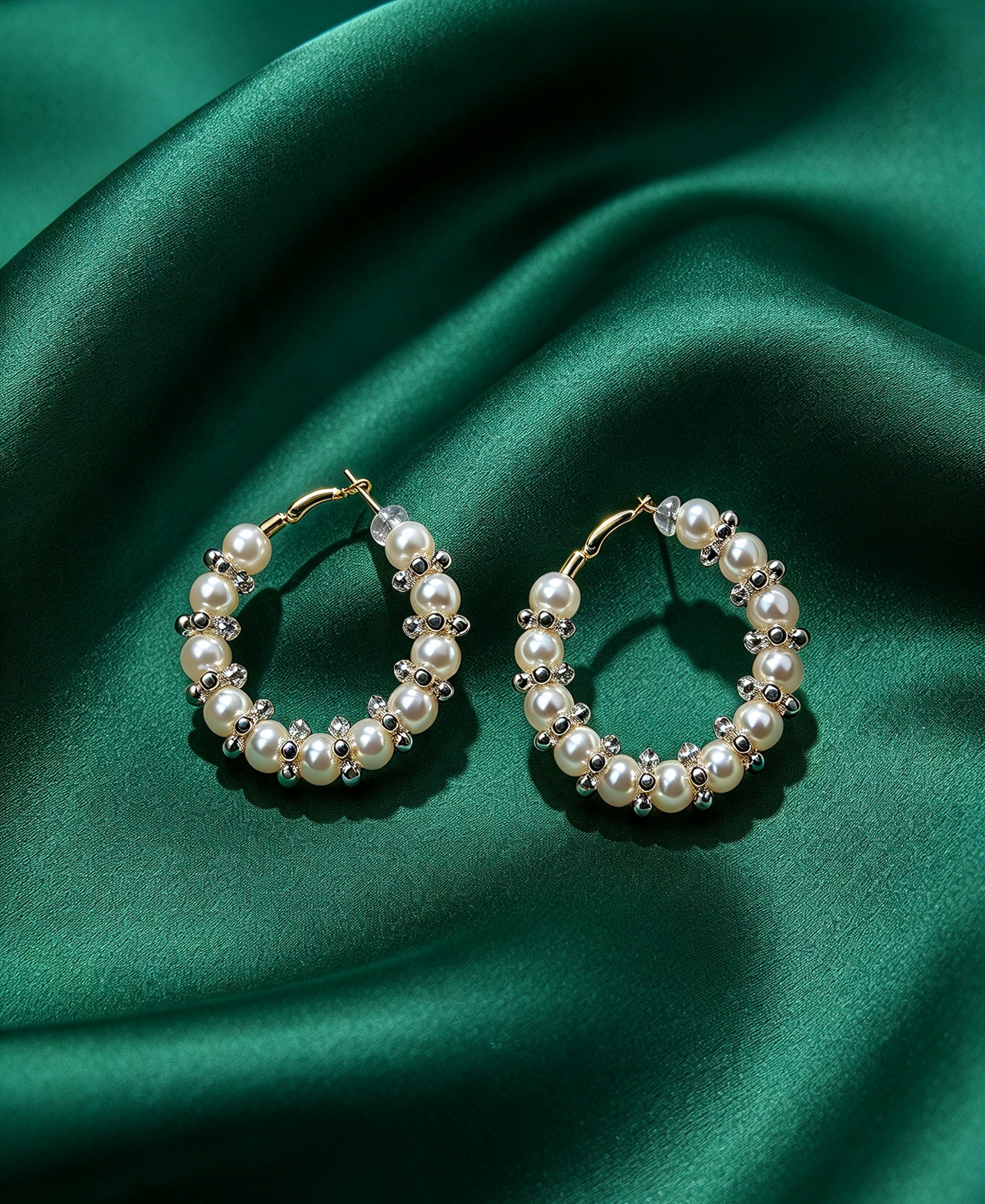 Pearl & clear crystal cluster hoop earrings, gold-tone lever-back, creamy white pearls with sparkling silver-toned crystal accents — resting on luxurious emerald green silk satin.