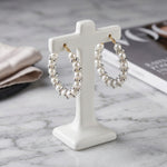 Pearl & clear crystal cluster hoop earrings, gold-tone lever-back, creamy white pearls with sparkling rhinestone accents — displayed on white ceramic stand, luxury jewelry presentation.