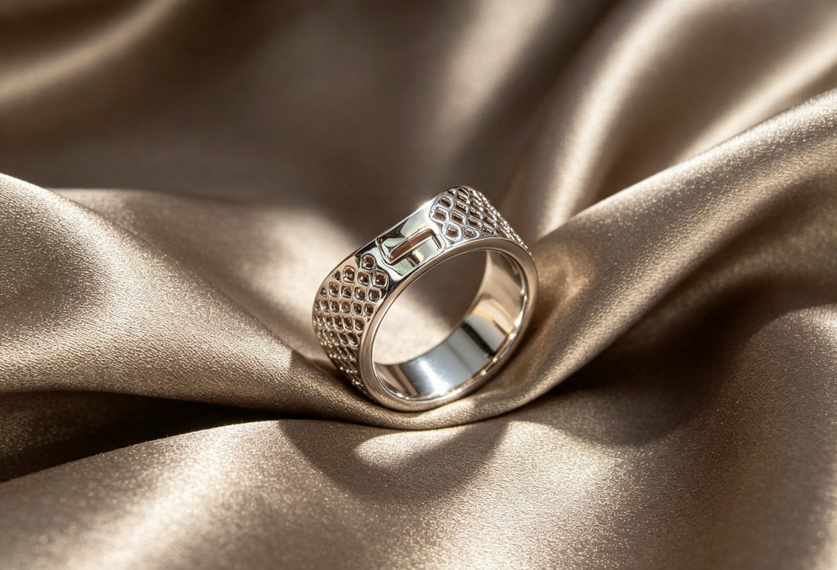 Premium polished silver-tone wide band ring with intricate geometric cut-out and honeycomb texture detailing, sleek modern design, smooth inner band, displayed on luxurious champagne satin fabric, elegant unisex jewelry.