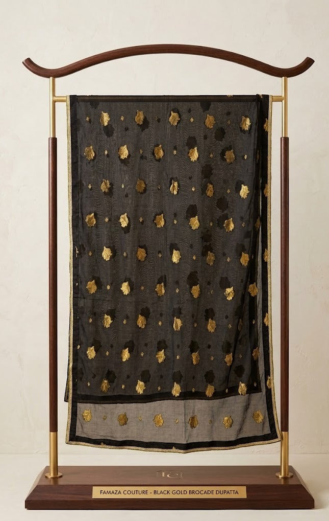 Black Banarasi chiffon dupatta adorned with intricate gold zari brocade motifs all over, featuring fine embroidered border and delicate detailing; displayed on an elegant wooden and gold stand, showcasing sheer luxurious fabric and traditional craftsmanship, perfectly matching the black silk kurta set.