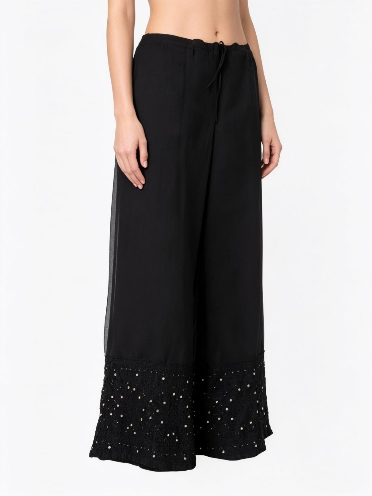 Close-up view of black georgette palazzo pants featuring detailed antique gold kaamdani work and traditional bakhiya embroidery, captured on a pure white background.