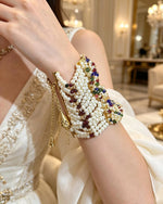 Luxurious gold plated wide cuff bangle featuring layered white pearls, vibrant Navratan gemstones, and delicate golden bell charms traditional South Asian bridal and festive statement jewelry.