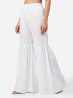 Close-up view of a model wearing premium white cotton sharara pants featuring an elasticated waistband, voluminous tiered flare, and intricate tonal Chikankari floral embroidery on the lower panels and hem.