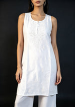 Medium close-up of a model wearing the white handcrafted sleeveless Chanderi silk Chikankari co-ord set, showcasing the fine embroidery detail against a solid dark backdrop.