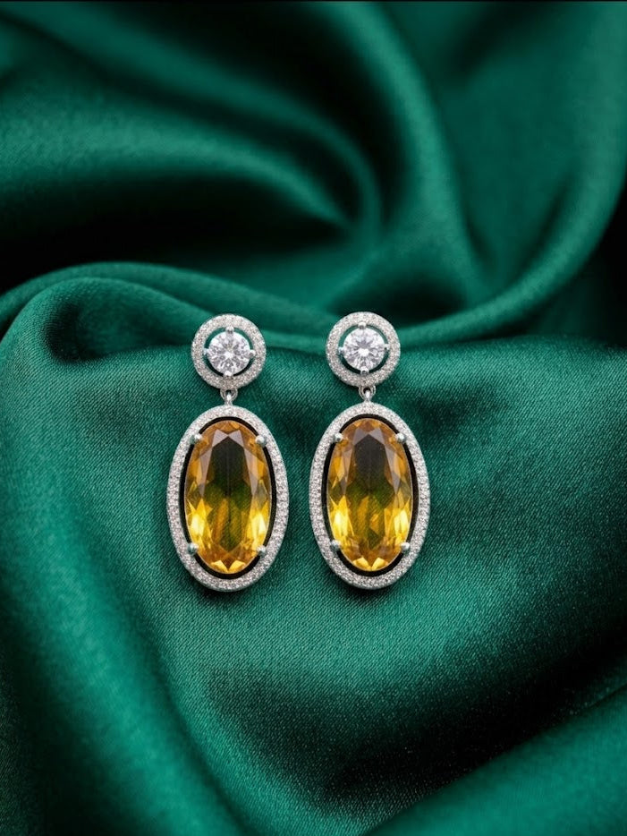 Pair of sterling silver two-tone gradient oval citrine drop earrings with diamond halos and round diamond studs on green satin.