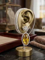 Elegant oval citrine gemstone earring with a diamond halo frame, presented on an ear-shaped stand for size reference.