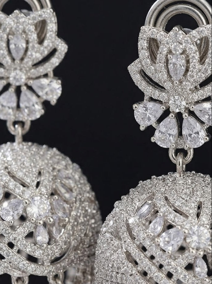 Silver-toned chandelier earrings heavily embellished with clear stones, shown in a close-up against a black background.