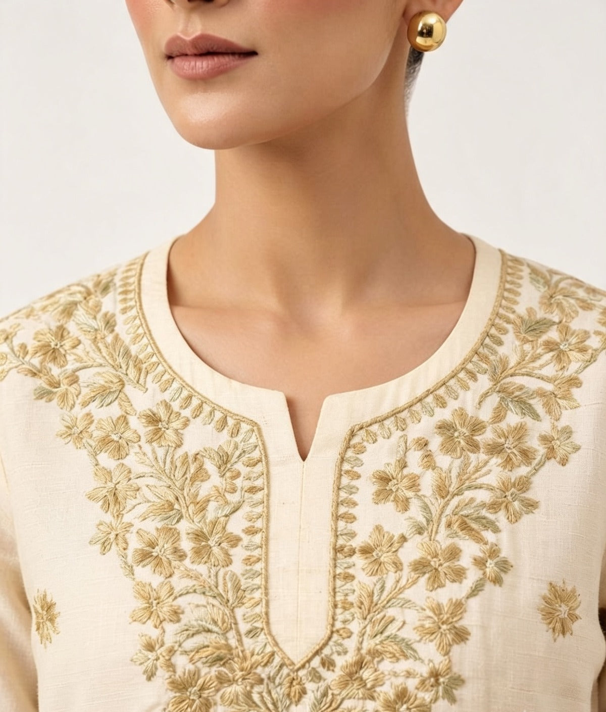 Close-up view of the neckline and yoke of a beige cotton short kurti featuring intricate gold thread floral embroidery and a keyhole neckline, worn without bottom wear.