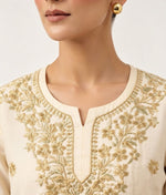 Close-up view of the neckline and yoke of a beige cotton short kurti featuring intricate gold thread floral embroidery and a keyhole neckline, worn without bottom wear.