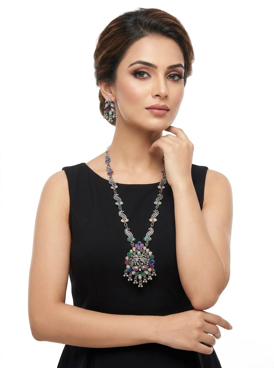 A model wearing an antique oxidized silver long necklace and matching earrings featuring a large peacock pendant and multicolor pastel stones.