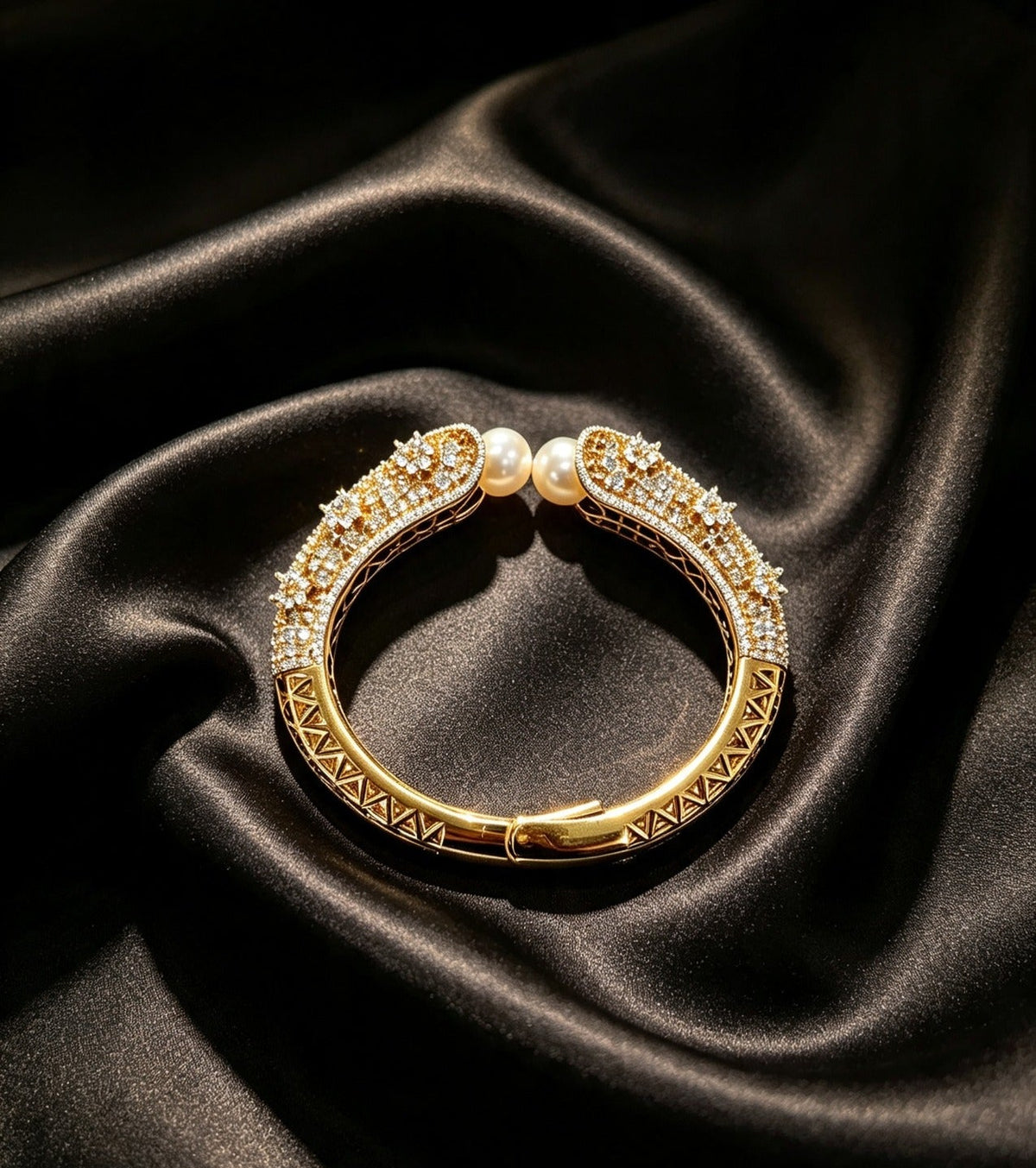 Famaza Couture gold-tone open cuff bracelet with two lustrous white pearls meeting at the opening, pavé-set clear crystals on curved ends, polished gold geometric lattice inner band with hinged clasp, elegantly displayed on luxurious black satin — premium couture statement jewellry.