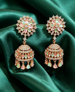Luxurious rose gold-plated floral CZ jhumka earrings with pastel pink and mint green stones displayed on rich emerald green silk fabric.