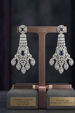 A detailed product photo of a single rose gold chandelier earring with an ornate, multi-tiered design, featuring numerous pavé-set clear diamonds and two prominent deep-blue cushion-cut sapphires, displayed against a dark background, with dimensions text at the bottom.