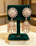 Close-up of rose gold-plated pastel pink and mint green floral CZ jhumka earrings displayed on a dark green velvet jewelry stand.