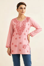 Front view of a model wearing a blush pink cotton short kurti featuring intricate matching pink floral embroidery, a keyhole neckline, and a square hem line, paired with matching trousers.