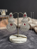 Luxury silver Chandbali earrings with brilliant white crystals and red ruby accents displayed on a white marble jewelry stand.