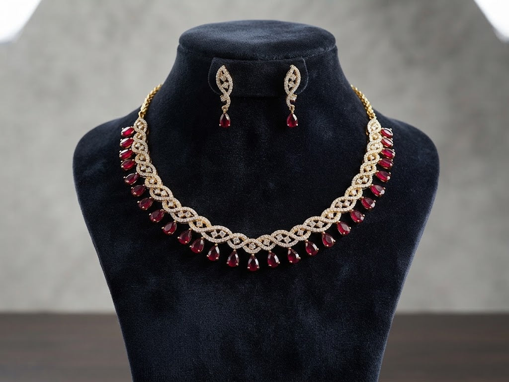 Gold-toned jewelry set displayed on a black velvet mannequin bust, featuring an ornate necklace with red teardrop stones and matching drop earrings.