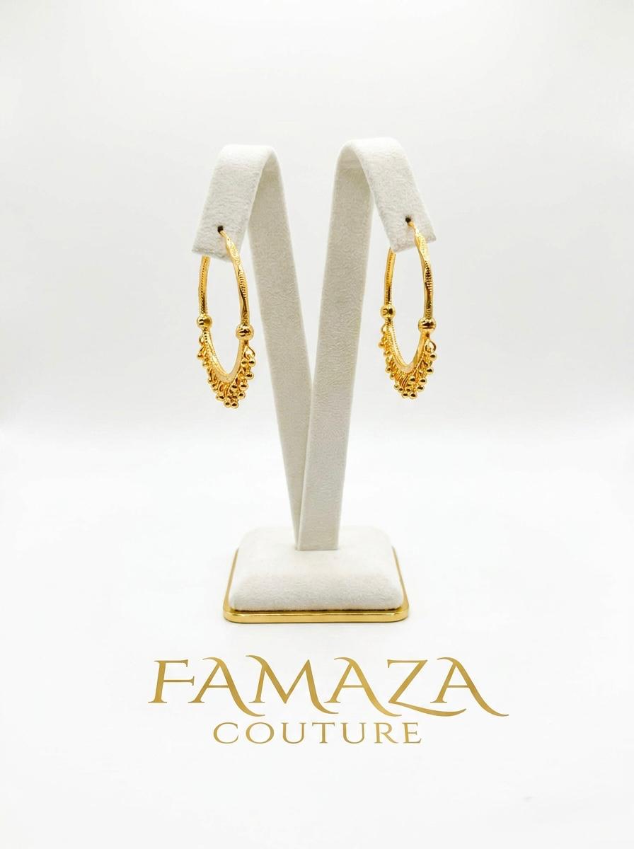 Pair of luxury gold-plated Bali hoop earrings featuring a crescent design with intricate gold bead drops, displayed on a posh white velvet stand for Famaza Couture.