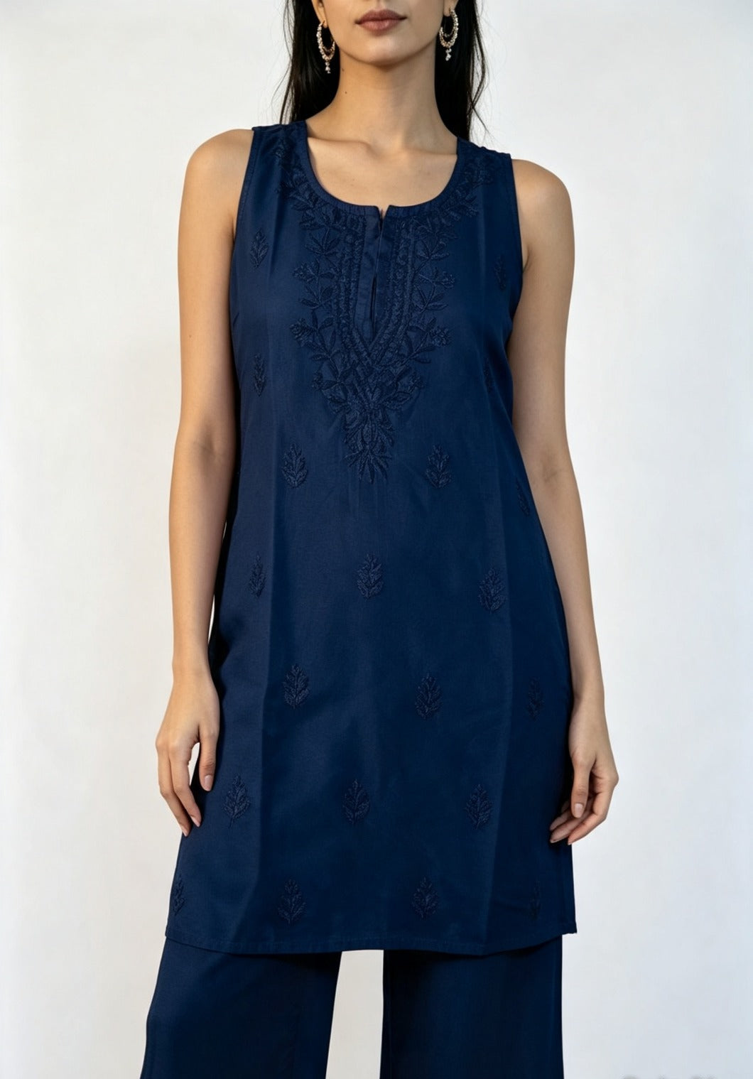 Medium close-up of a model wearing the navy blue handcrafted sleeveless Chanderi silk Chikankari co-ord set, emphasizing the delicate embroidery pattern on the front against a neutral white background.