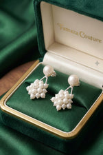 A pair of pearl cluster drop earrings displayed in an open green velvet jewelry box with a gold-tone border. The inside lid shows the brand name 'Aethelred & Co.