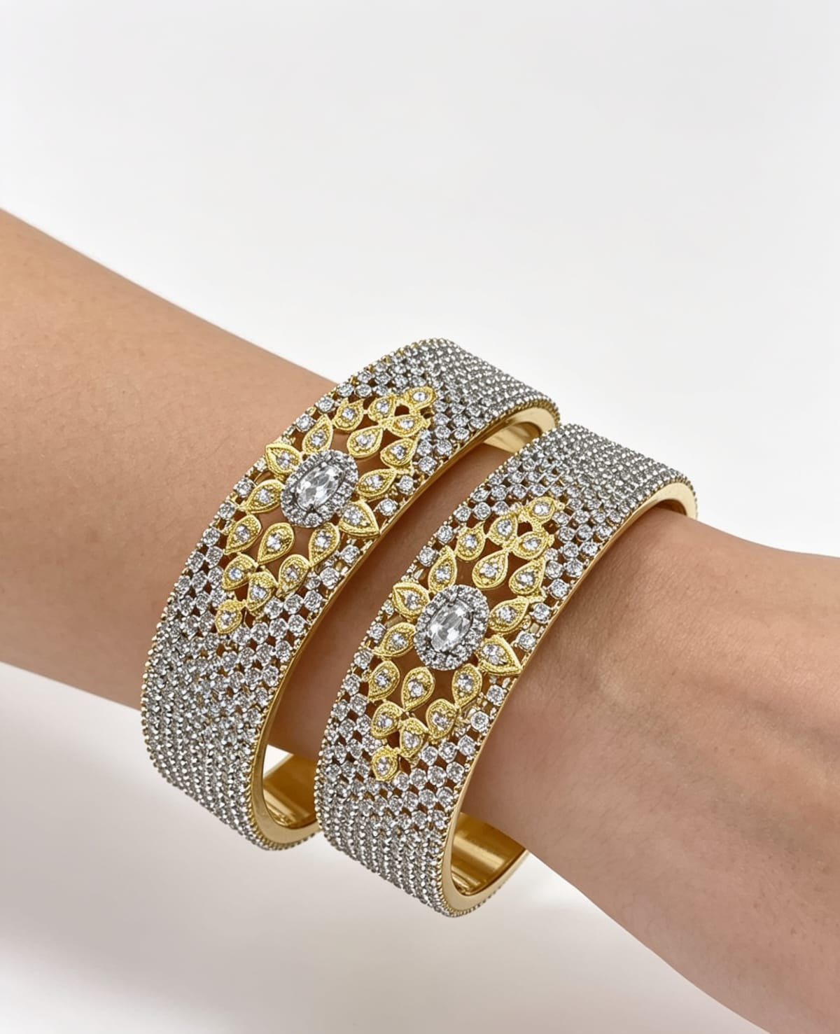 A model wearing a pair of luxury wide-band dual-tone bangles, featuring a full pavé American Diamond surface with an intricate gold floral centerpiece.