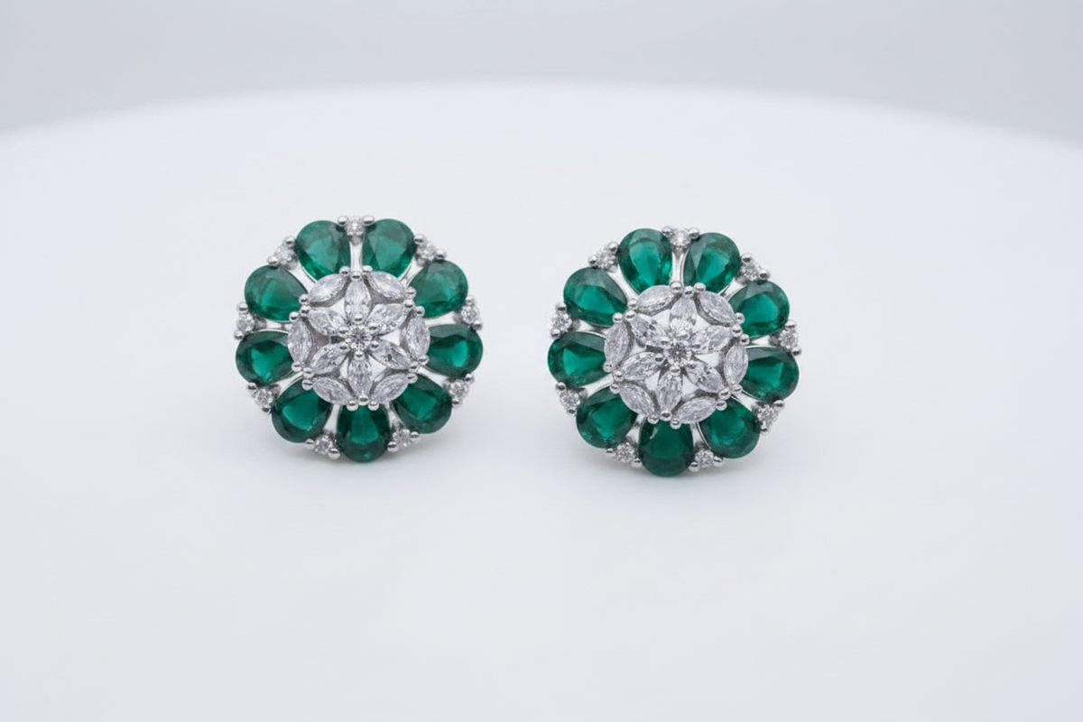 A pair of round floral cluster stud earrings featuring green emerald-cut gemstones and a central clear round stone in a silver-toned setting, displayed on a clean white background.