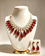 Luxury ruby red teardrop statement necklace and earring set, vibrant red pear gemstones with brilliant CZ crystal accents, premium jewelry presentation on cream velvet stands, ideal for weddings and upscale festive occasions.