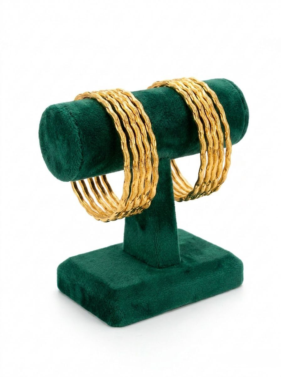 A set of 8 micro gold-plated copper bangles with a textured twisted rope design, displayed on a posh emerald green velvet T-bar jewelry stand against a crisp white background