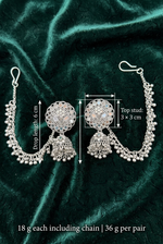 Silver-toned traditional Indian jhumka earrings with detailed filigree and dangling bead chains, displayed on a dark green velvet background with measurement annotations.