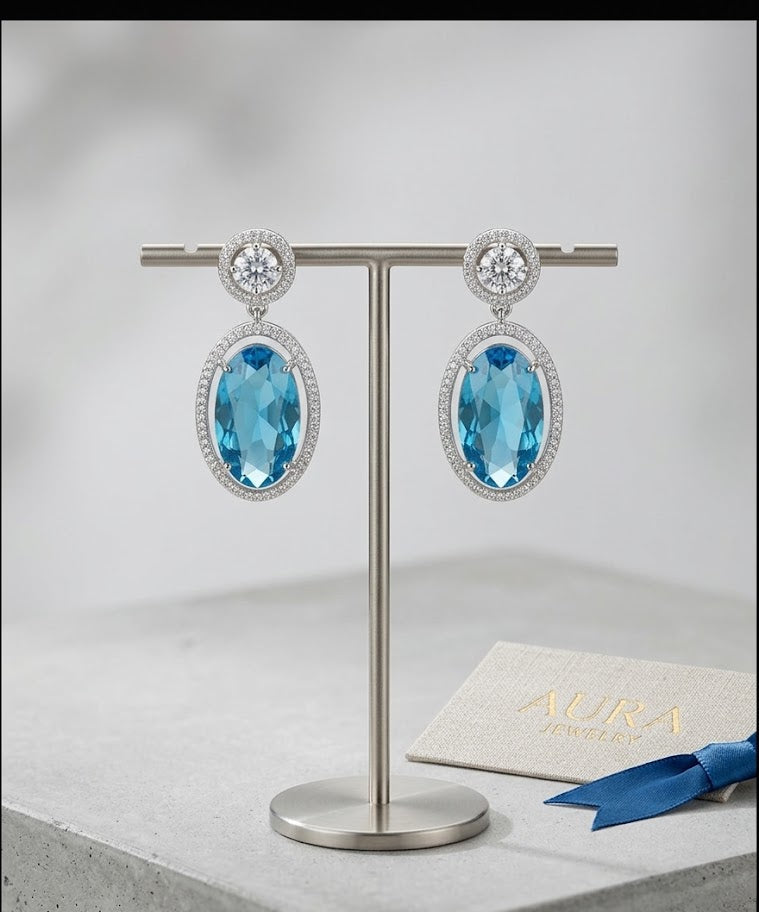 Luxury oval blue crystal earrings with diamond halo setting on a jewelry stand, professional product photography for fine fashion accessories.