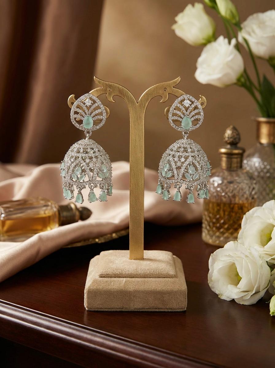 Silver-toned bridal Jhumka earrings with high-shine ice blue crystal encrustation and hanging crystal droplets on a display stand.