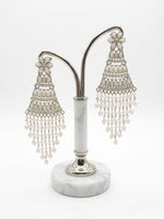 Silver filigree work and iridescent teardrop accents on elegant pearl statement earrings on stand.