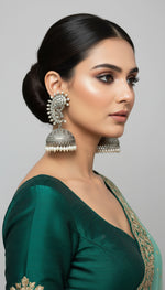 Hand holding ornate silver earrings with kundan stone and silver jhumka in the bottom