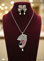 Silver plated a set of peacock-shaped pendant in silver chain with peacock-shaped earrings. The pendant is detailed with blue enamel and has sparkling crystal white AD and hot pink stones embellishments. Party wear jewellery set. Jewellery set is displayed on a black velvet jewellery dummy. Party wear set.