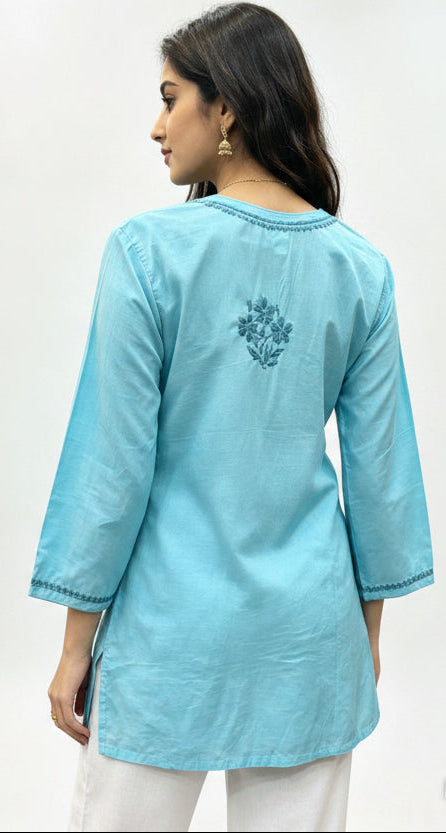 A model shown from the back, wearing a sky blue cotton short kurti with matching embroidery around the neckline and a floral motif on the upper back, against a white studio background.