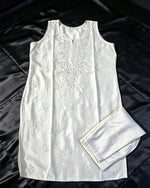 Flat lay view of the white handcrafted sleeveless Chanderi silk Chikankari tunic and matching folded trousers arranged on a black satin surface.