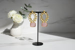Statement earrings featuring an coral pink sugar stone with detailed floral carvings and golden accents on a stand.
